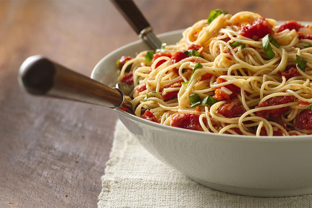 A bowl of pasta with fresh tomatoes and two utensils in it