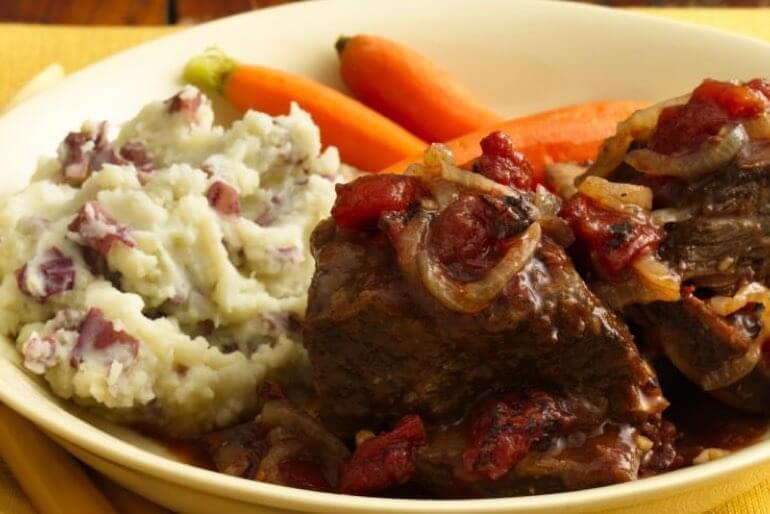 Beef short ribs recipe with tomato wine sauce plated with a side of carrots and mash.
