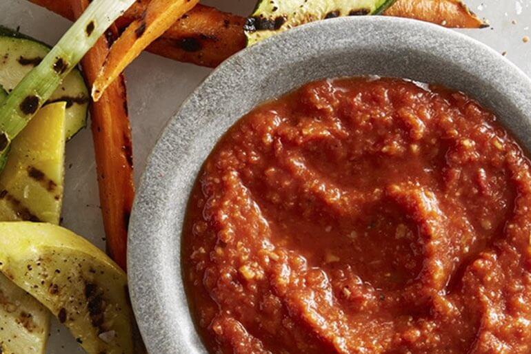 Smoky romesco sauce recipe served in a grey bowl with a side of grilled vegetables.