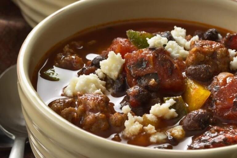Black bean chorizo chill recipe with organic diced tomatoes topped with mexican cheese in a white bowl.