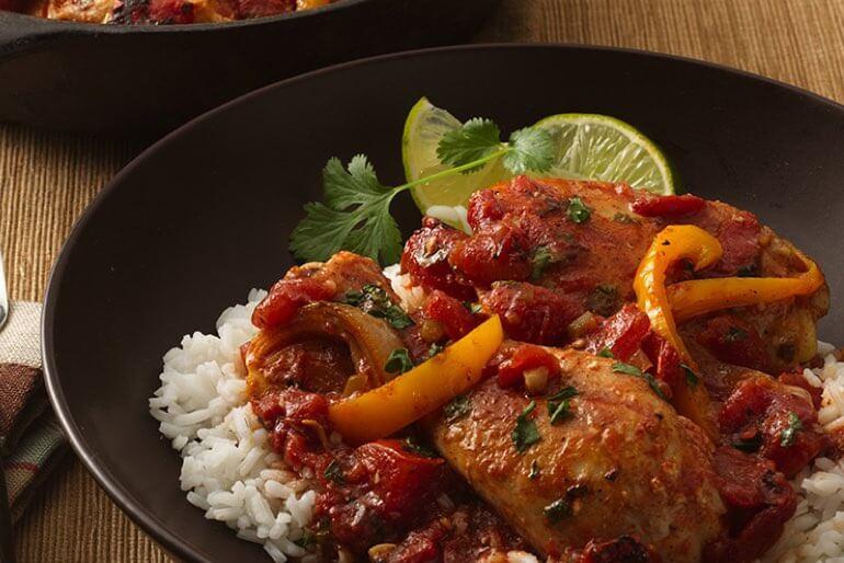 Braised chicken in tomato sauce recipe with chopped yellow bell pepper, garnished with cilantro and a side of lime.
