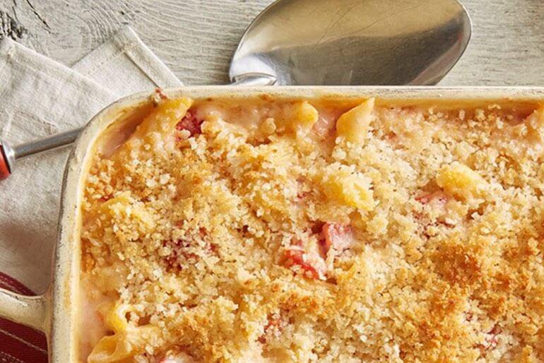 Grilled mac and cheese recipe with chopped tomatoes served in a cream-coloured casserole dish.