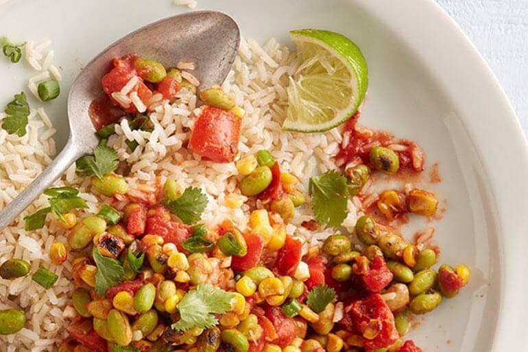 Vegan summer succotash recipe with diced tomatoes, corn, green onion and garlic served on white rice with a wedge of lime.