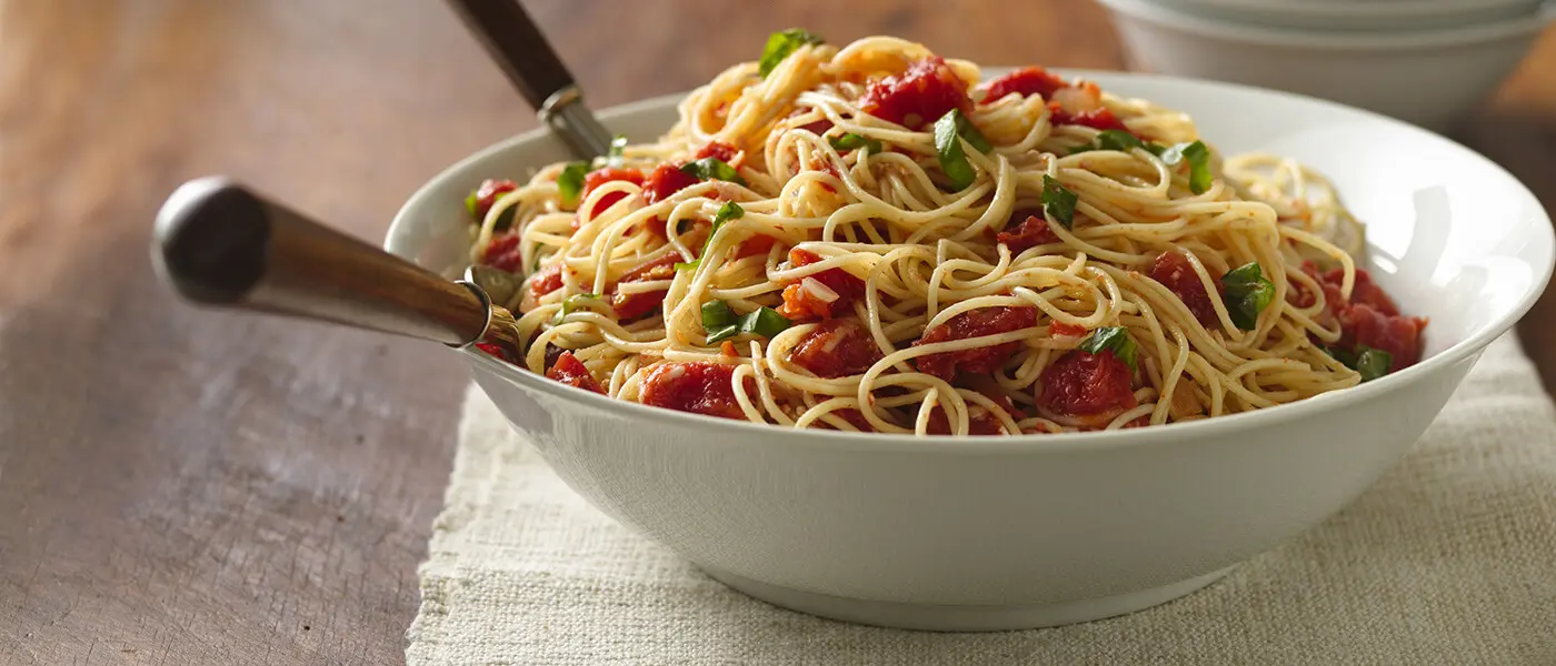 Angel hair pasta recipe with tomato and basil served in a white bowl.