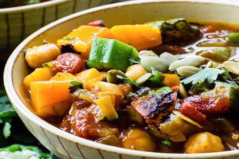 Recette africaine de ragoût de tomates et de potiron servie dans un bol, avec du potiron haché, des tomates grillées et du gombo.