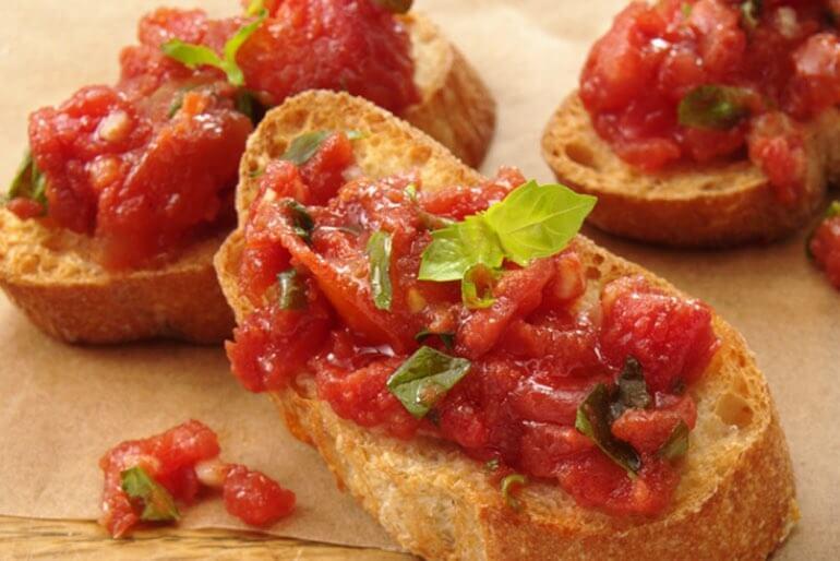 Bruschetta with diced tomatoes and basil recipe served on a wooden chopping board.