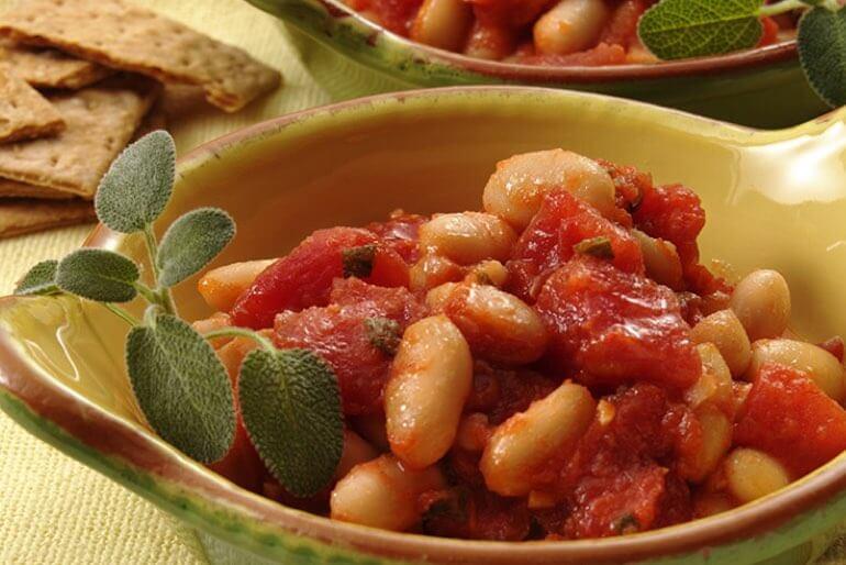 Cannellini bean recipe with diced tomatoes and sage served in a green bowl with a sprig of sage.