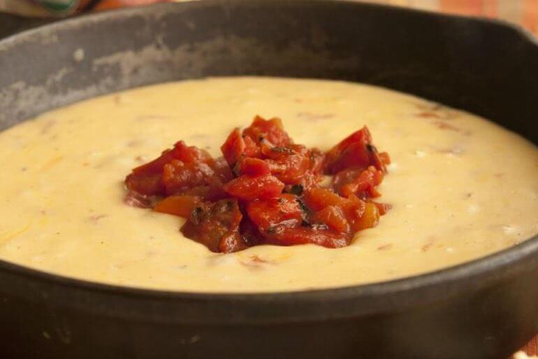 Recette de dip de queso aux chipotles servie dans un bol noir et garnie de tomates en dés.