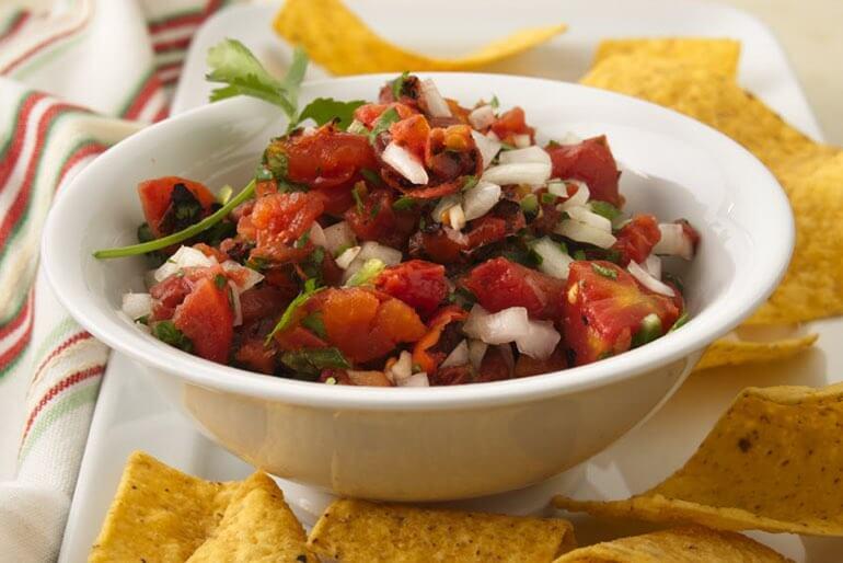 Recette de salsa de tomates grillées à la flamme avec de la coriandre et du citron vert, servie dans un bol blanc avec des chips tortilla.