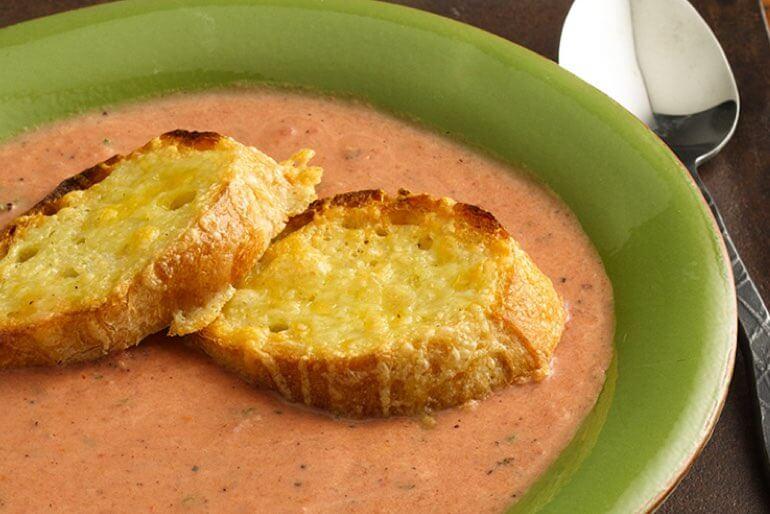 Recette de soupe de tomates grillées au feu de bois, servie dans un bol vert avec du pain au fromage.