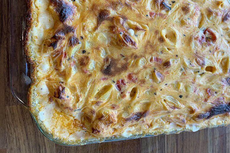 Recette de macaronis au fromage cuits au four avec des tomates grillées au feu de bois, servis dans une cocotte en verre.