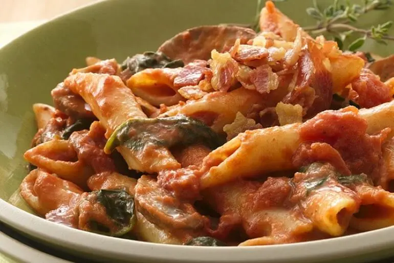 Recette de pâtes Penne à la sauce tomate et aux champignons, garnie de bacon et agrémentée d'une branche de thym.