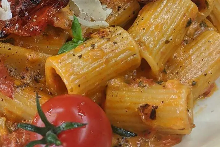 Recette de Rigatoni au basilic et à la rose, garnie d'une tomate cerise et de feuilles de basilic.