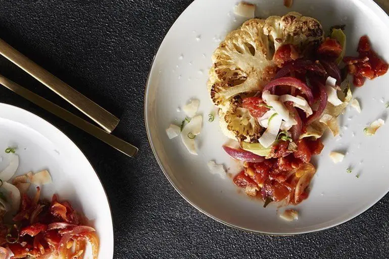 Roasted cauliflower steak recipe with tomato chutney on two white plates.