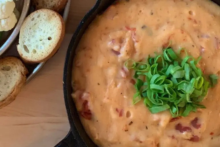 Recette de fondue au fromage avec tomates hachées, garnie d'échalotes hachées.