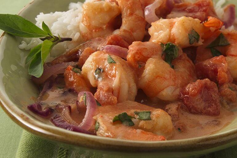 Recette thaïlandaise de crevettes saisies à la sauce tomate, basilic et noix de coco servie dans une assiette verte avec du riz.