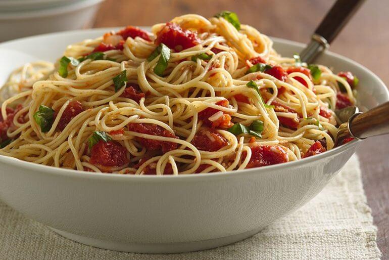 Angel hair pasta recipe with tomato and basil served in a white bowl.