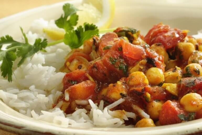 Chickpea and tomato curry on rice recipe garnished with cilantro and a wedge of lemon, served in a white bowl.