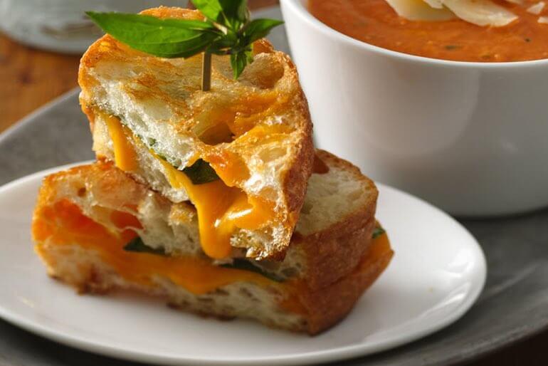 Fire roasted tomato grilled cheese recipe garnished with basil and served with a side of tomato soup.