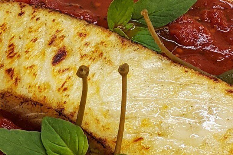 Seared halibut recipe with fire roasted tomato sauce and basil leaves.