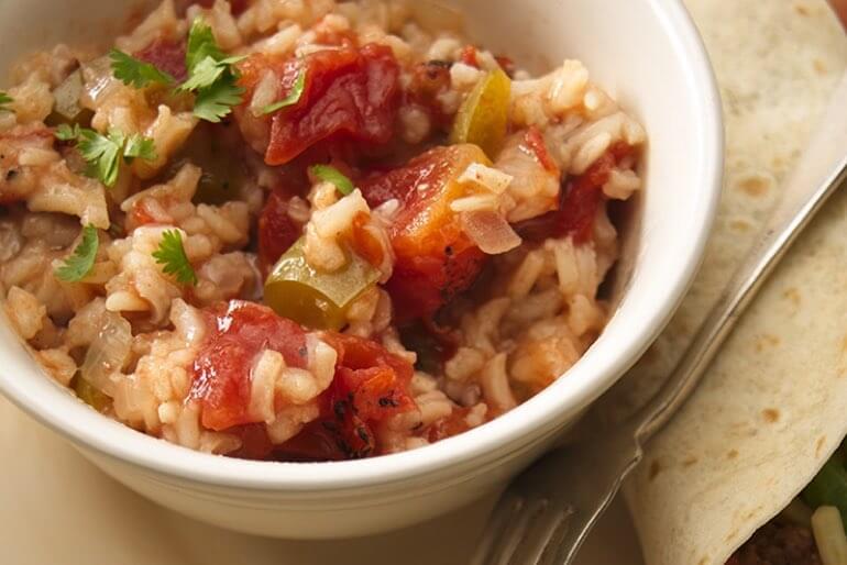 Spanish rice recipe with diced tomatoes, green bell pepper, and onion served in a white bowl with a side of tortilla.