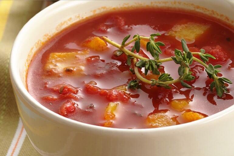 Sweet pepper soup with roasted sweet pepper served in a white bowl and garnished with a sprig of thyme.